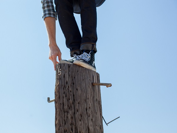 młody człowiek balansujący na pionowym ściętym drzewie